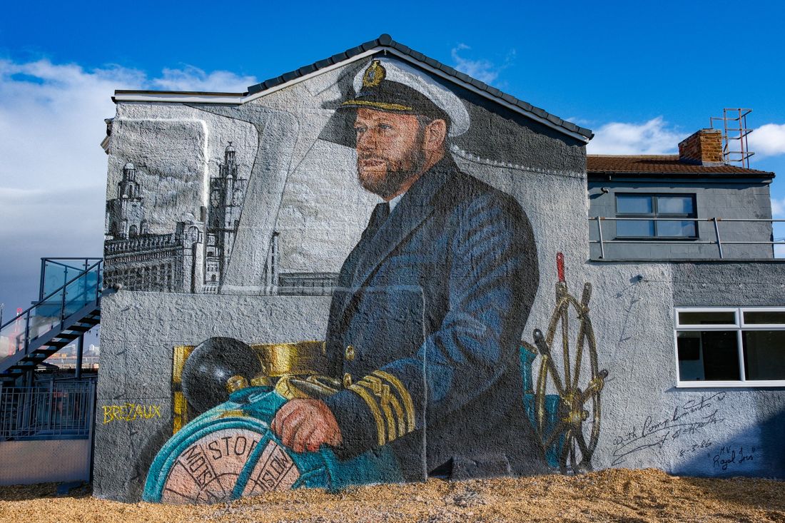 The Captain Mike Lowe mural by Brezaux on the gable end of the Master Mariner in New Brighton: Mike in his white-topped cap and braided jacket, his hand on the telegraph, the ship's wheel beside him and the Liver Building behind.