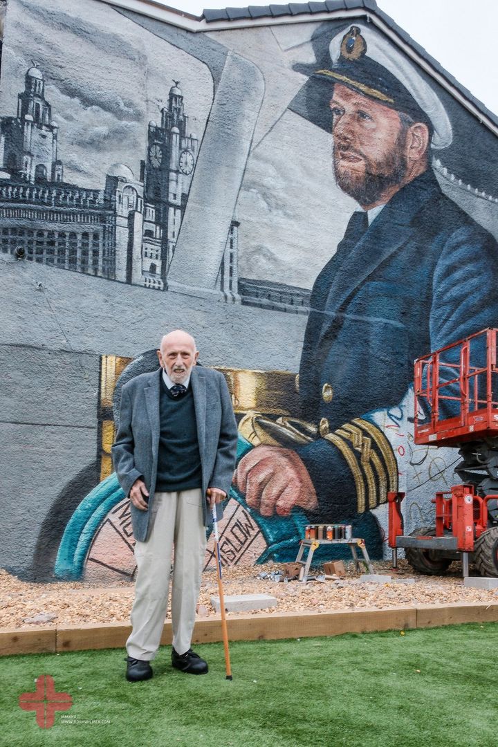 Mike Lowe standing with a walking stick in front of the finished mural.